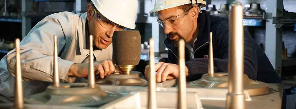 Two men with protective headgear examining a metal casting setup, with a Foseco employee providing application guidance to a customer in an industrial environment