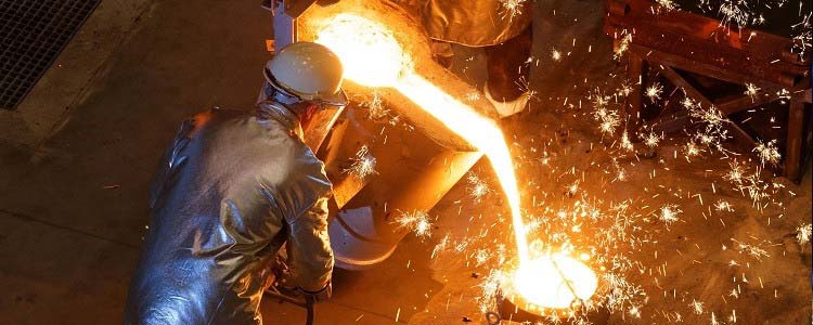 Overhead view of a foundry worker in protective gear pouring molten metal from a furnace into a mold, with bright sparks flying around the intense and fiery work environment.